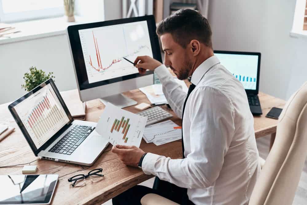 inspirado para trabalhar duro jovem empresario em trajes formais comparando dados usando o computador enquanto esta sentado no escritorio