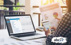 mulher mexendo no celular enquanto a tela do notebook está aberta no ERP omega da ABC71 indicando a automação de relatórios ERP fiananceiros